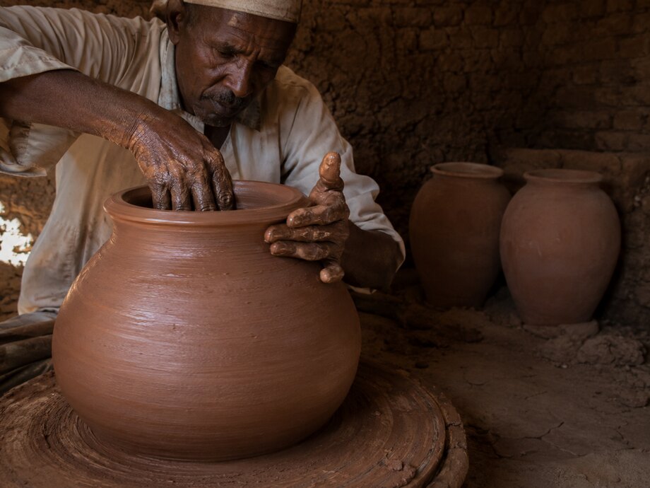 A potter shaping a clay vessel on the wheel