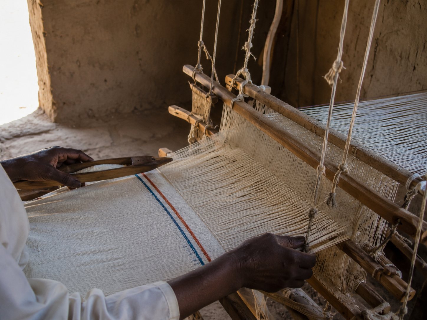Hands weaving cotton cloth on a wooden loom